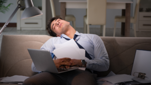 A professional asleep on their couch with their laptop still open, symbolizing the exhaustion and blurred boundaries between work and personal life.