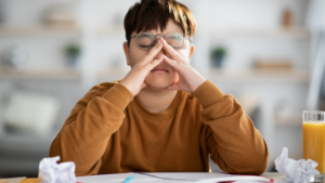 A child sitting at a desk, hands on their face in frustration, surrounded by crumpled papers, symbolizing the overwhelming feeling of tackling tasks.