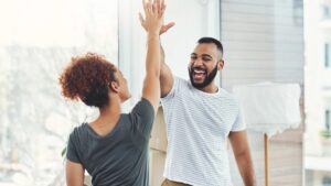 A man and woman smiling and high-fiving, celebrating a shared success with genuine joy and mutual support, symbolizing owning achievements and embracing confidence without guilt.