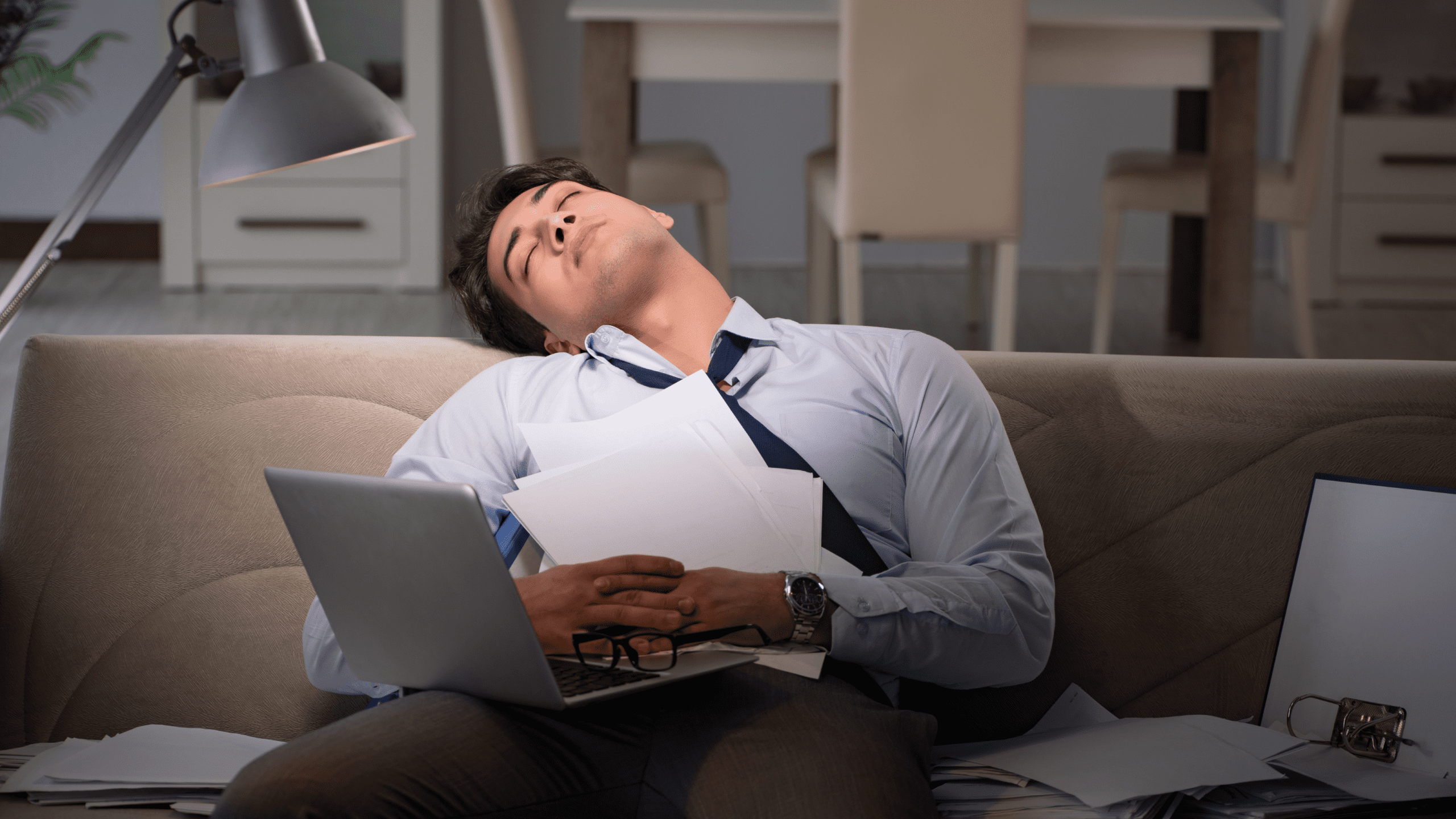 A professional asleep on their couch with their laptop still open, symbolizing the exhaustion and blurred boundaries between work and personal life.